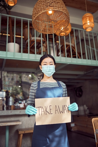 Foto del personale del bar in maschera medica e guanti di gomma che tengono striscione da asporto all'interno della caffetteria