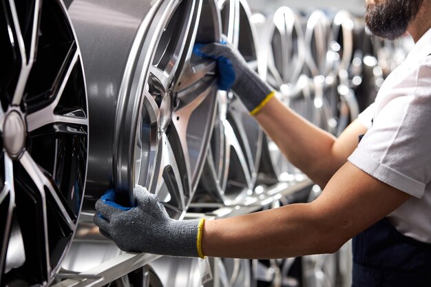 Foto del primo piano del maschio in guanti che prendono i cerchi automatici dal rack, meccanico auto ritagliata in uniforme al lavoro