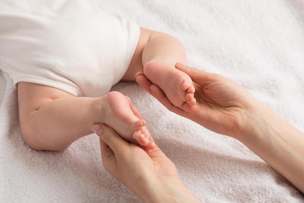 Foto del primo piano del neonato sdraiato sullo stomaco e sulle mani della madre che tengono le gambe minuscole su uno sfondo tessile bianco isolato