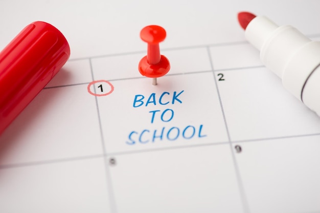 Foto del primo piano del segno sul calendario alla prima iscrizione blu di ritorno a scuola con puntina da disegno rossa e pennarello