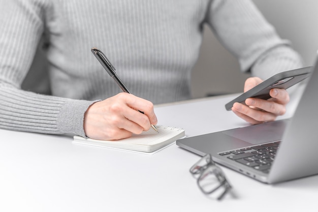 Foto del primo piano della donna che lavora con il computer portatile e che scrive in taccuino.