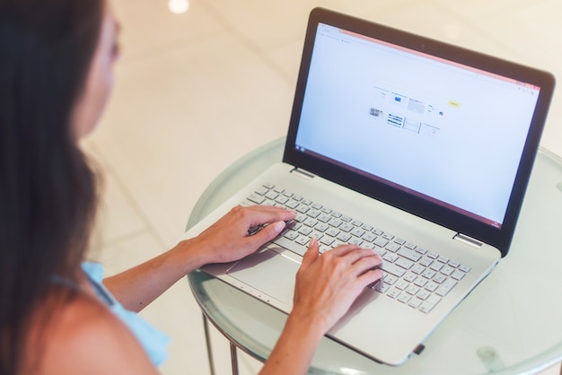 Foto del primo piano della donna giovane di affari che lavora al computer portatile in ufficio bianco.