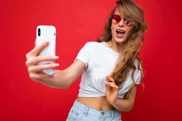 Foto del primo piano della persona di sesso femminile bionda adulta sexy che tiene il telefono cellulare che prende la foto del selfie usando