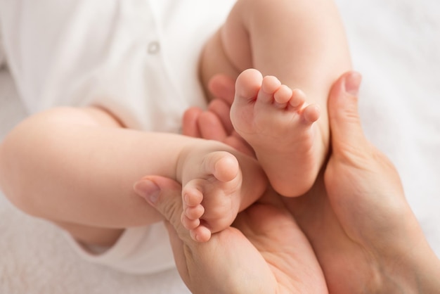 Foto del primo piano delle mani della madre che tengono i piedini del neonato su fondo tessile bianco isolato