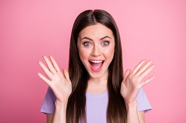 Foto del primo piano di attraente divertente signora scioccata buon umore sorridente denti lunghi pettinatura bocca aperta ascoltare belle notizie alzare le braccia indossare casual t-shirt viola isolato sfondo di colore rosa pastello