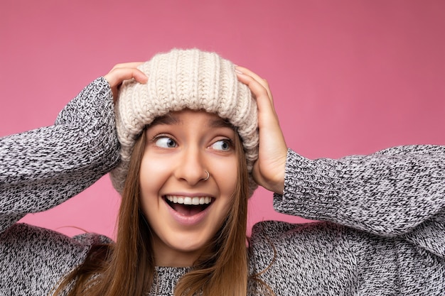 Foto del primo piano di attraente positiva scioccata stupita giovane donna bionda scura isolata sopra la parete di sfondo colorato indossando abiti alla moda di tutti i giorni guardando al lato che mostra le emozioni facciali.