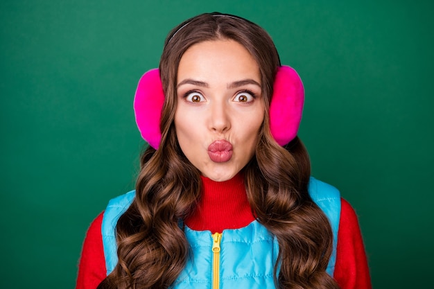 Foto del primo piano di bella carina pazza giovane donna imbronciata labbra inviare aria bacio lungo separazione fidanzato quarantena indossare scaldaorecchie rosa gilet con zip blu maglione rosso isolato sfondo di colore verde