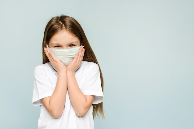 Foto del primo piano di un bambino allegro piuttosto positivo durante la quarantena covid19 che indossa una maschera respiratoria blu su sfondo blu