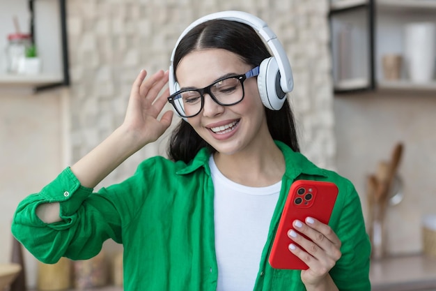 Foto del primo piano felice giovane bella femmina in abiti verdi e occhiali per ascoltare musica in bianco