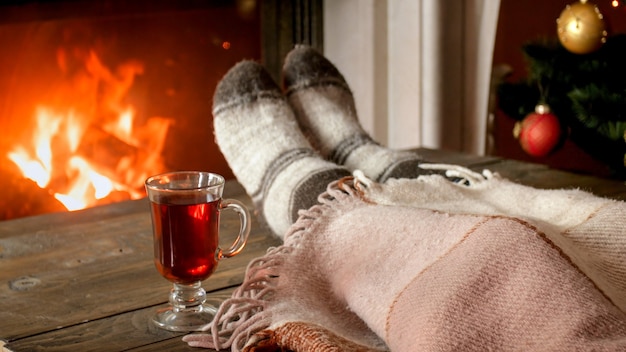 Foto del primo piano giovane donna che beve il tè sotto la coperta accanto al caminetto