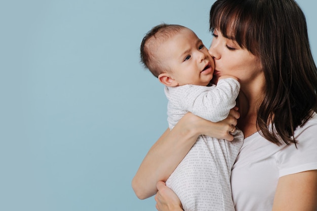 Foto del primo piano. La madre amorevole abbraccia il bambino e lo bacia, tenendolo tra le braccia, molto spazio per il tuo testo