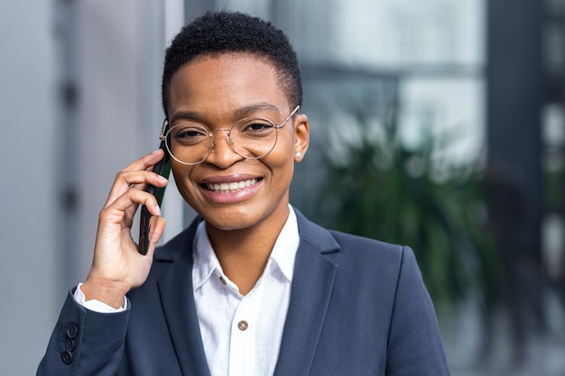 Foto del ritratto ravvicinato di giovane donna d'affari bella, donna afroamericana che parla al telefono, sorridente e gioendo felice guardando la fotocamera