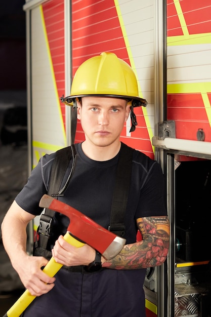 Foto del vigile del fuoco che indossa il casco con l'ascia contro l'autopompa antincendio