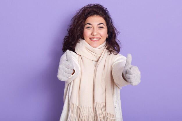 Foto dell'interno di giovane donna sveglia mora adorabile positiva che fa gesto, mostrando segno eccellente con due mani