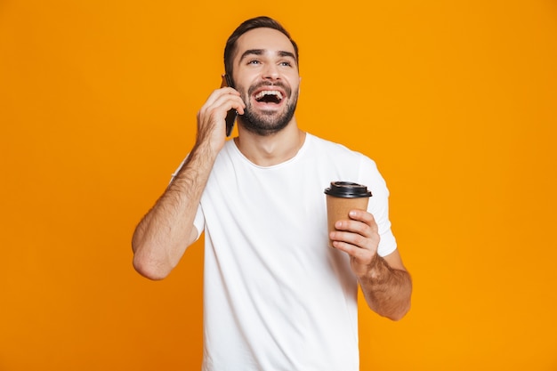 Foto dell'uomo caucasico 30s in abbigliamento casual che parla sul telefono cellulare mentre beve il caffè da asporto, isolato