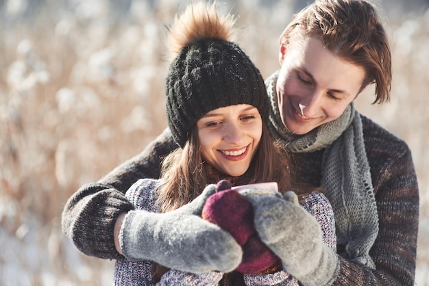 Foto dell'uomo felice e della donna graziosa con le tazze all'aperto nell'inverno. Vacanze invernali e vacanze