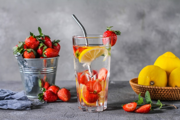 Foto della bevanda fredda ghiacciata di estate rinfrescante. Acque infuse alla fragola. Acqua minerale con fragole fresche limone con uno sfondo grigio. Acqua disintossicante con limone e fragola. Copia spazio.