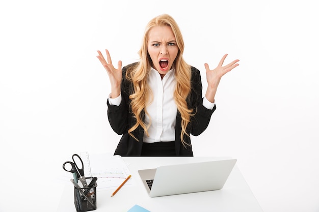 Foto della donna di affari sconvolta che si siede alla tavola e che lavora al computer portatile, isolata