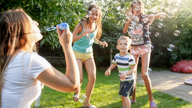 Foto della famiglia felice che gioca con le bolle di sapone nel giardino del cortile della casa. La famiglia gioca e si diverte all'aperto in estate