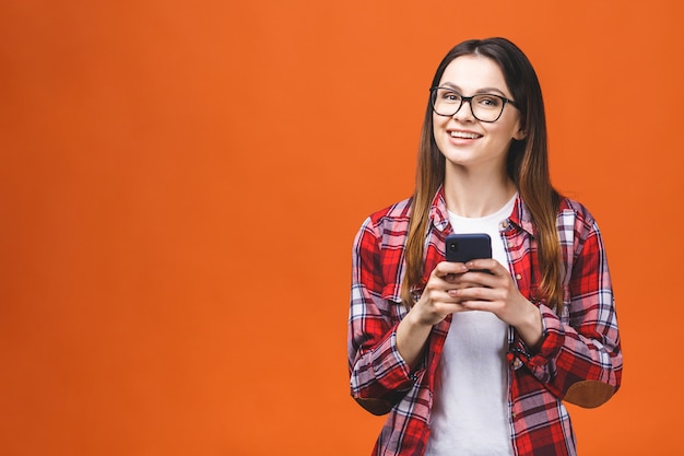 Foto della giovane donna sveglia allegra che chiacchiera dal telefono cellulare isolato sopra il fondo arancio della parete.