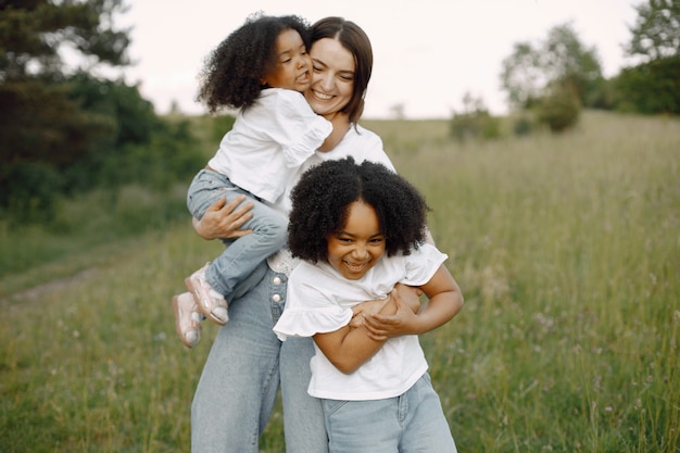 Foto della madre caucasica e delle sue due figlie afroamericane che si abbracciano insieme all'aperto. Le ragazze hanno i capelli ricci neri