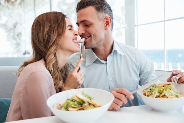 Foto delle coppie romantiche felici cenando e mangiando i salati insieme, mentre riposando nel caffè della città durante la pausa pranzo