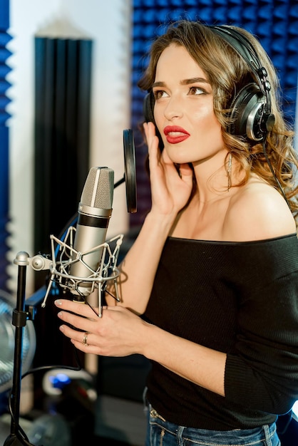 Foto dello studio di bella donna con capelli ricci e labbra rosse in camicia nera elegante che posa con il microfono. Concetto di canto.