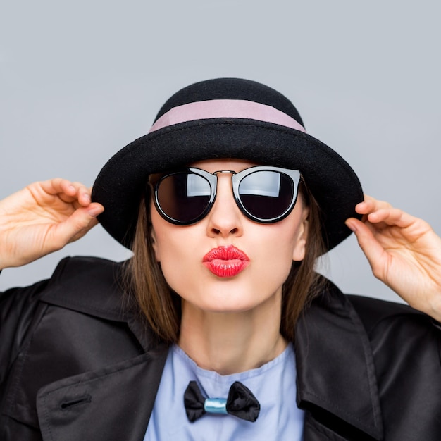 Foto dello studio di moda della signora alla moda in cappello e occhiali da sole donna che indossa cappello e impermeabile