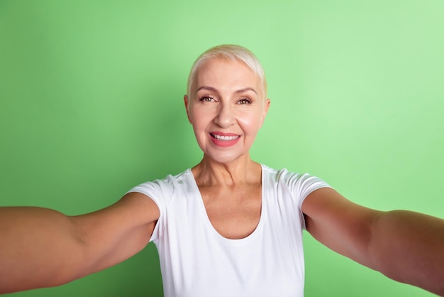 Foto di allegra donna invecchiata fare selfie registrare video vacanze blog isolati su sfondo di colore verde.