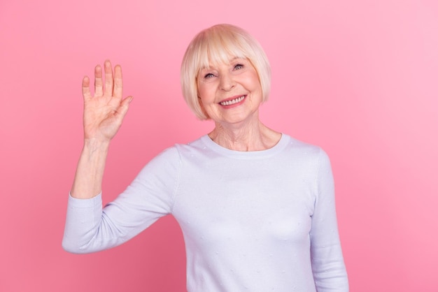 Foto di allegra donna matura buon umore agitando la mano ciao incontrare amici isolati su sfondo rosa