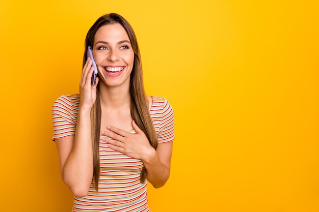 Foto di attraente bella signora tenere le mani del telefono parlando con il migliore amico ascoltare scherzi divertenti pettegolezzi voci indossare maglietta a righe casual isolato parete di colore giallo