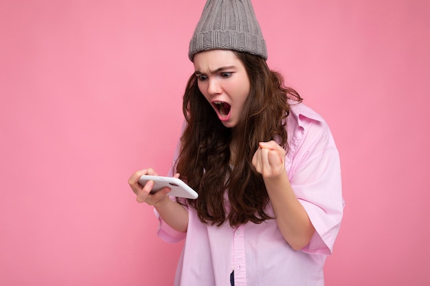 foto di attraente emotiva giovane donna bruna che indossa elegante camicia rosa e cappello grigio isolato