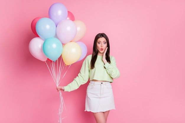 Foto di attraenti amiche scioccate organizzano una festa di compleanno a sorpresa molti palloncini d'aria inaspettati indossano casual pullover verde raccolto jeans minigonna isolato sfondo rosa color pastello