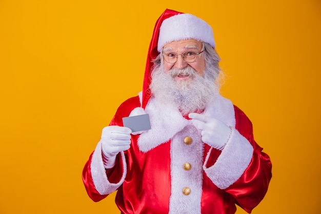 Foto di Babbo Natale in possesso di una carta di credito su sfondo giallo. Concetto di pagamento facile con carta di credito o di debito. pagamento bancario