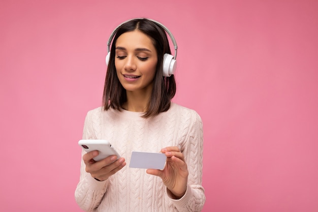 Foto di bella giovane donna castana felice che porta il maglione casuale rosa isolato sopra il colore rosa