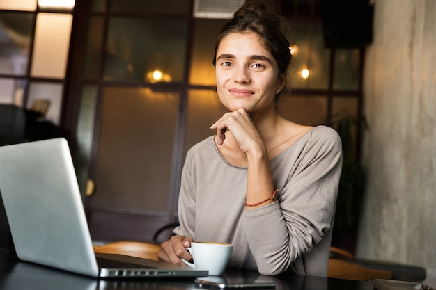 Foto di bella giovane donna seduta in un caffè al chiuso utilizzando il computer portatile.