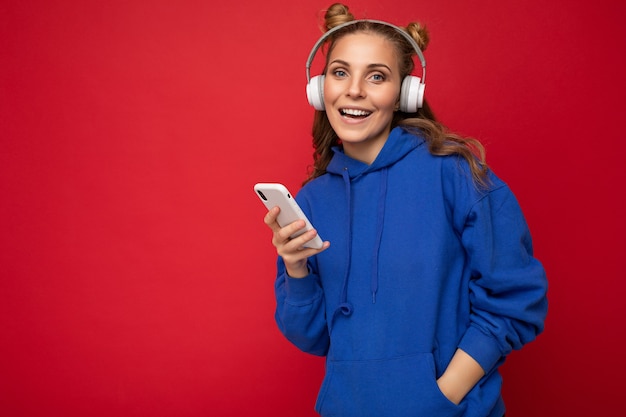 Foto di bella giovane donna sorridente felice che indossa una felpa con cappuccio blu elegante isolata sopra il rosso