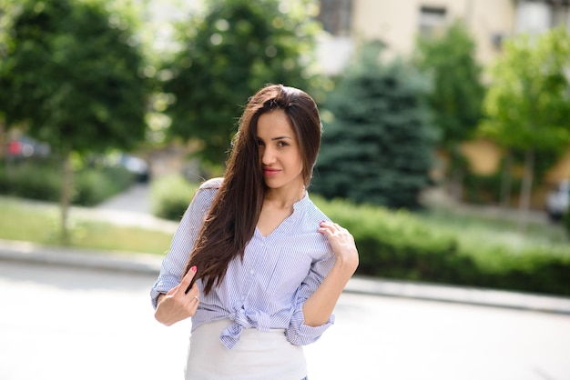 Foto di bella giovane donna sorridente tocco capelli ricci lunghi bruna parco a piedi indossare top bianco all'aperto