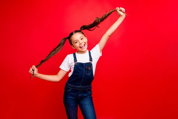 Foto di bella piccola signora umore positivo vacanze di capodanno che iniziano tenendosi per mano giocando con le code lunghe indossare jeans casual t-shirt bianca complessiva isolato sfondo di colore rosso