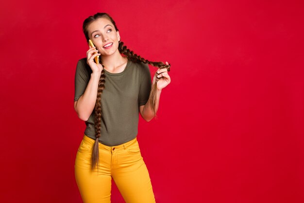 Foto di bella signora che tiene le mani del telefono parlando con gli amici discutere di notizie fresche pettegolezzi voci indossare pantaloni gialli casual t-shirt verde isolato colore rosso sfondo