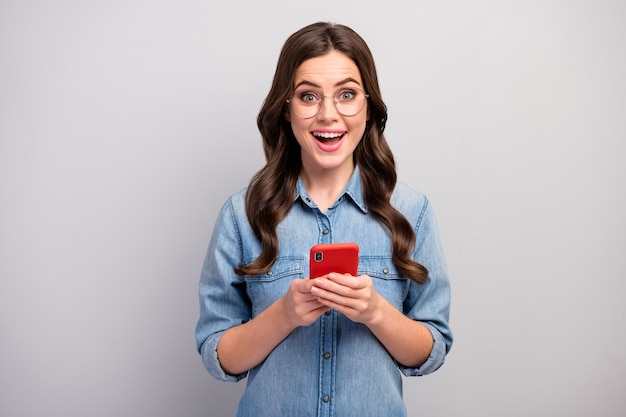 Foto di bella signora di affari che passa in rassegna il telefono controlla i seguaci abbonati tossicodipendenti utente bocca aperta indossare specifiche jeans casual camicia di jeans isolato colore grigio