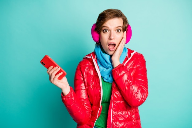 Foto di bella signora matta bocca aperta tenere il telefono mano sullo zigomo bot credere che molti seguaci indossano sciarpa cappotto rosso copri orecchie rosa ponticello verde isolato parete color verde acqua