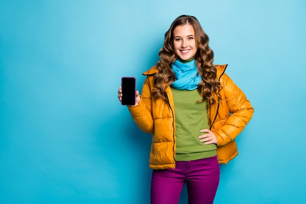 Foto di bella signora tenere le mani del telefono consigliando nuovo gadget smart phone modello basso prezzo di vendita indossare giallo soprabito sciarpa viola pantaloni ponticello verde isolato blu parete di colore