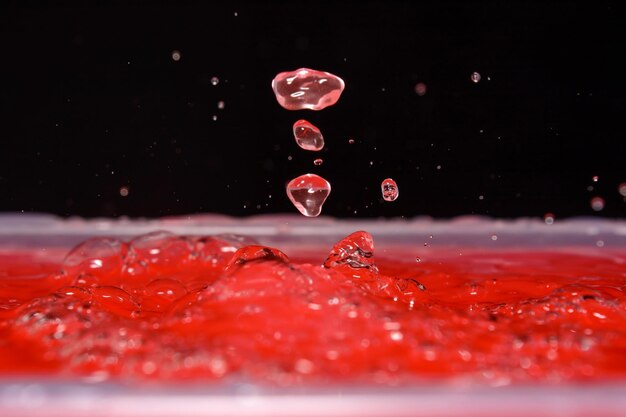 Foto di belle gocce d'acqua rosse che cadono sull'acqua e schizzi sullo sfondo nero