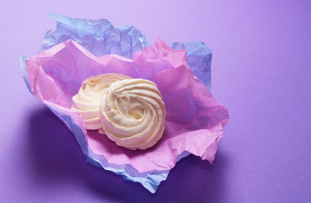 Foto di cibo di zephyr fatto in casa, marshmallow in carta da imballaggio viola. Dessert dolce sano su uno sfondo rosa.