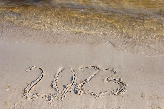 Foto di concetto di nuovo anno I numeri dell'anno 2023 sono scritti a mano sulla superficie della sabbia del mare Onda morbida del mare e spiaggia sullo sfondo