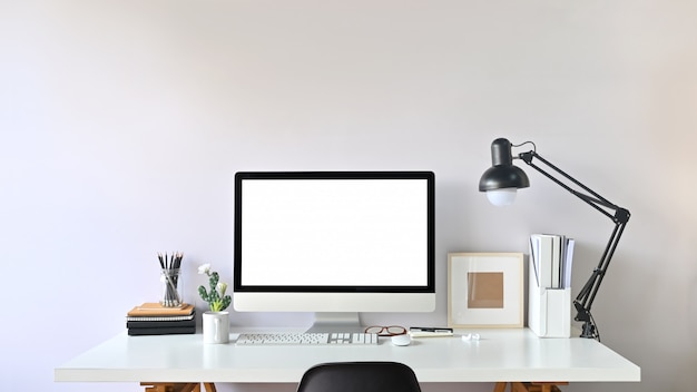 Foto di Contemporary Workspace. Monitor bianco dello schermo in bianco sullo scrittorio funzionante moderno. Attrezzature sul tavolo. Concetto di ufficio moderno.