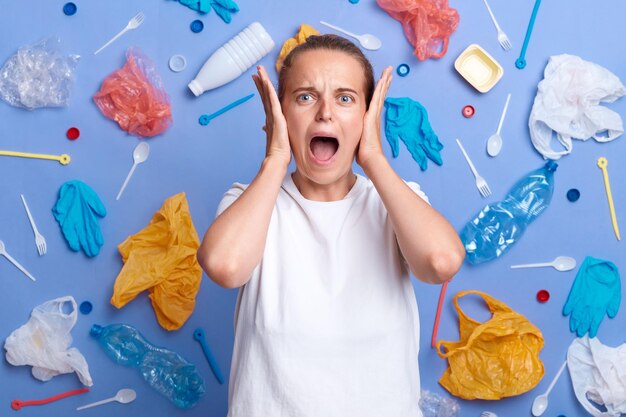 Foto di disperazione donna infelice raccolse rifiuti di plastica isolati sulla parete blu essendo scioccata dall'inquinamento della Terra urlando tiene la bocca aperta vuole risolvere il problema dell'inquinamento ambientale