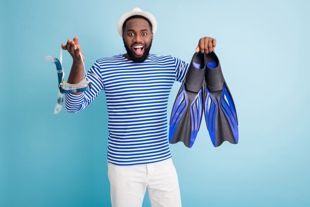 Foto di divertente pelle scura ragazzo tenere dispositivi subacquei pinne tubo occhiali maschera eccitato per iniziare ad affondare indossare berretto da sole bianco camicia da marinaio a strisce pantaloncini isolato muro di colore blu