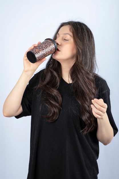 Foto di donna bruna con i capelli lunghi che beve da una tazza.